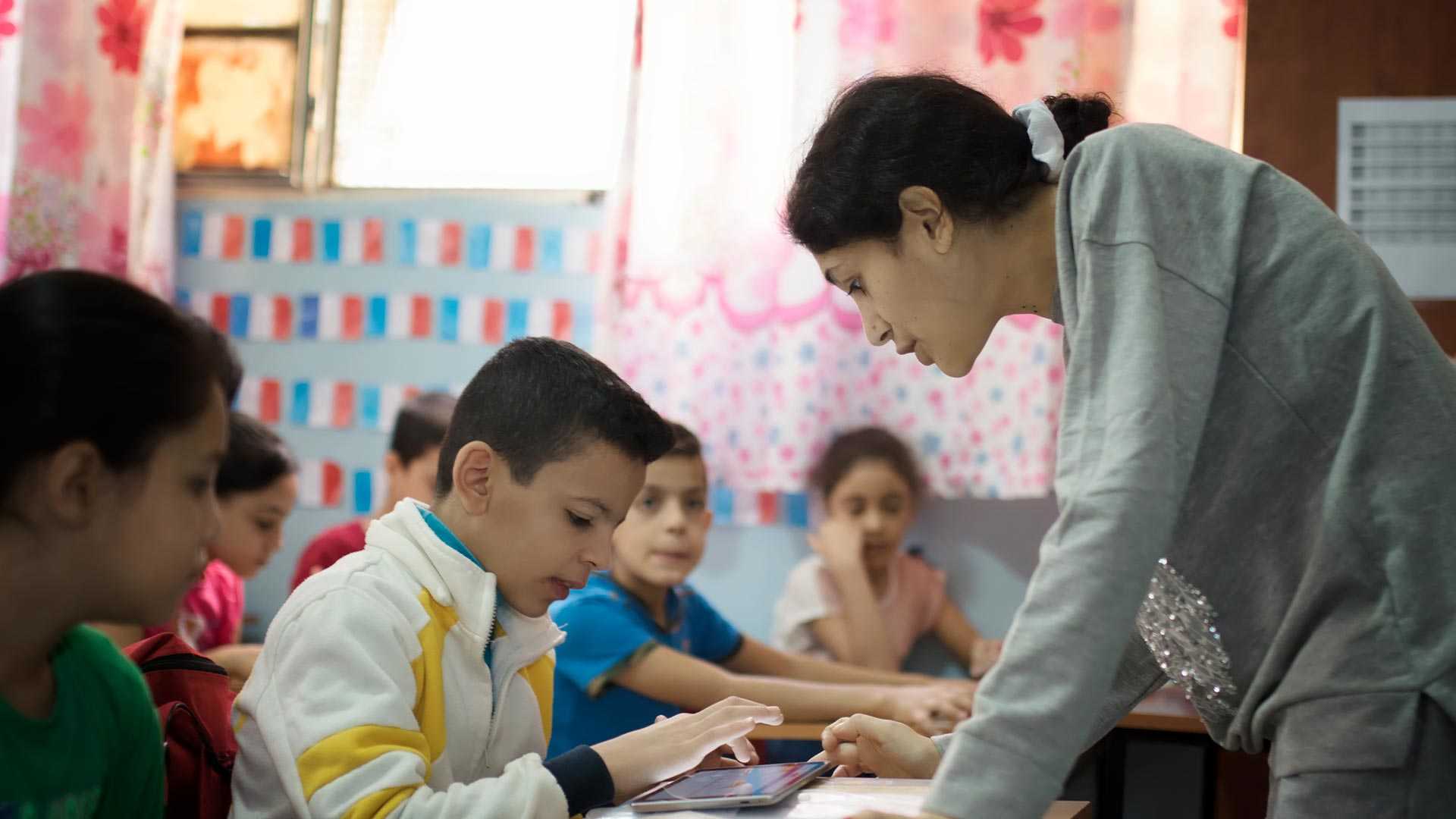 A teacher providing guidance to a class of children learning using tablets